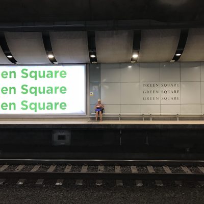 S2FM0A A woman sitting on a bench on the platform reading a book as she waits for her train at Green Square train station in Sydney, Australia